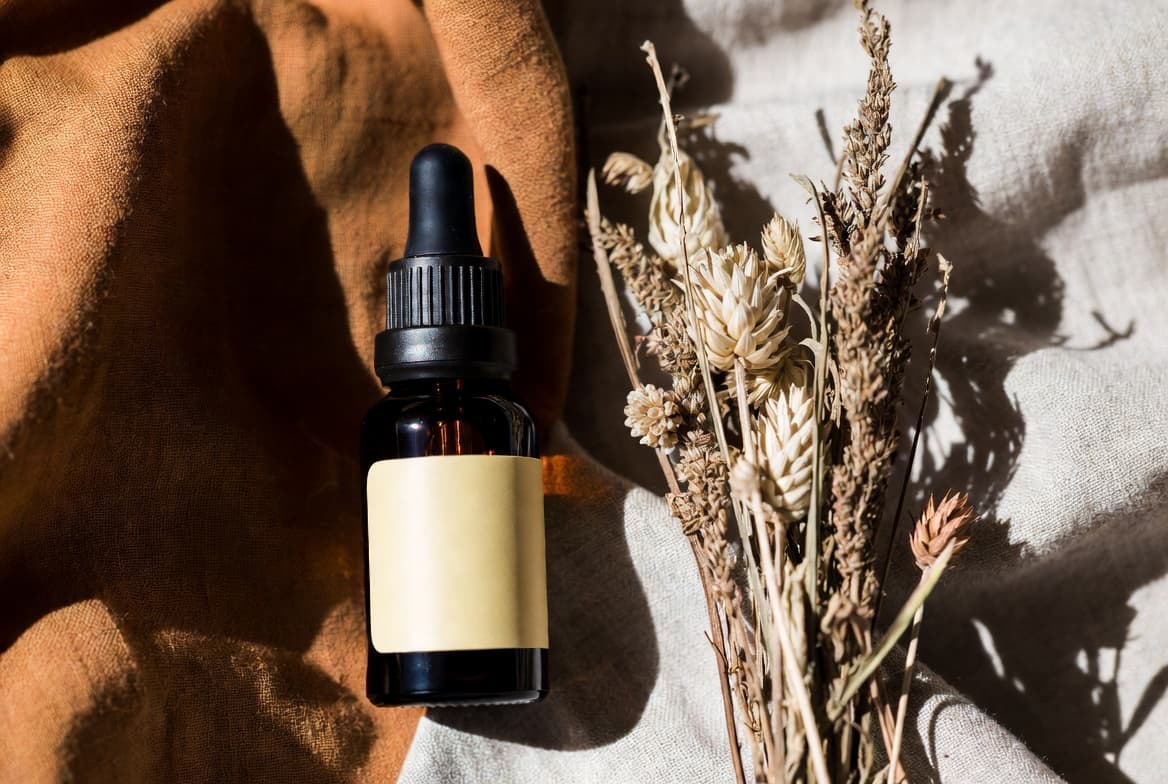 Amber glass dropper bottle of body oil beside dried wildflowers on linen