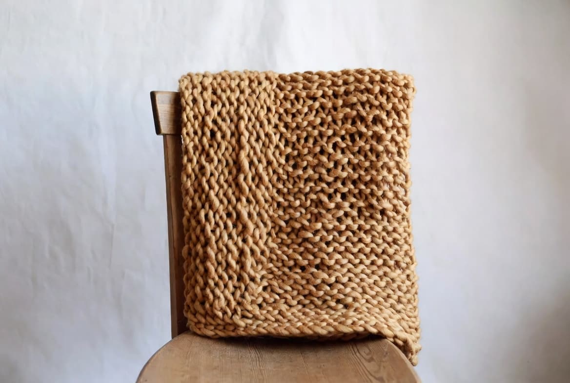 Chunky oatmeal knit throw draped over a wooden chair