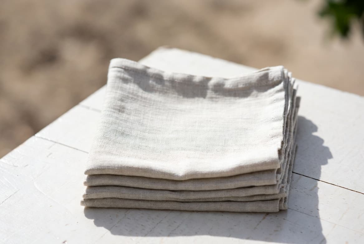 Folded ivory linen napkins stacked on a white table in sunlight