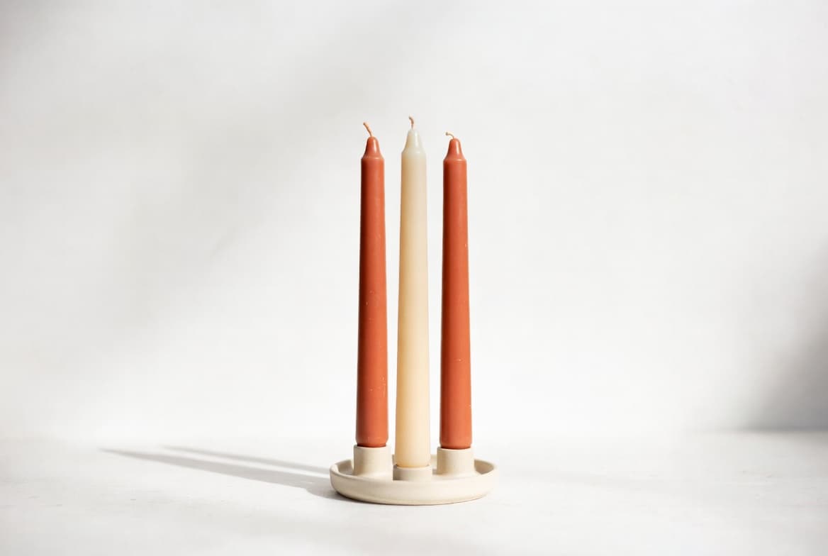 Three taper candles in terracotta and cream in a ceramic holder on a white surface